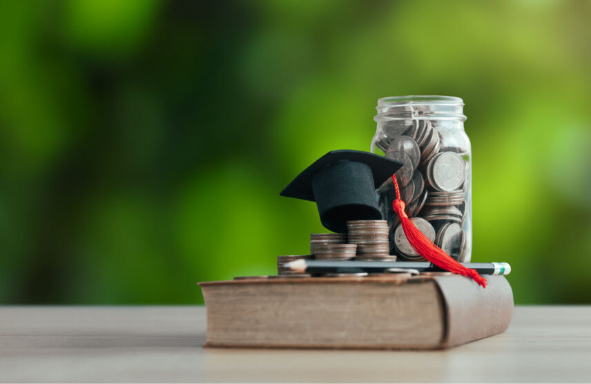 Jar of coins, a book, and graduation cap laying on top.