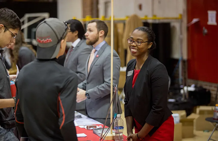 How to navigate a college fair. Image of college rep at a booth, talking to a high school student.