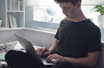 Crafting the perfect college application. Male student working on laptop.